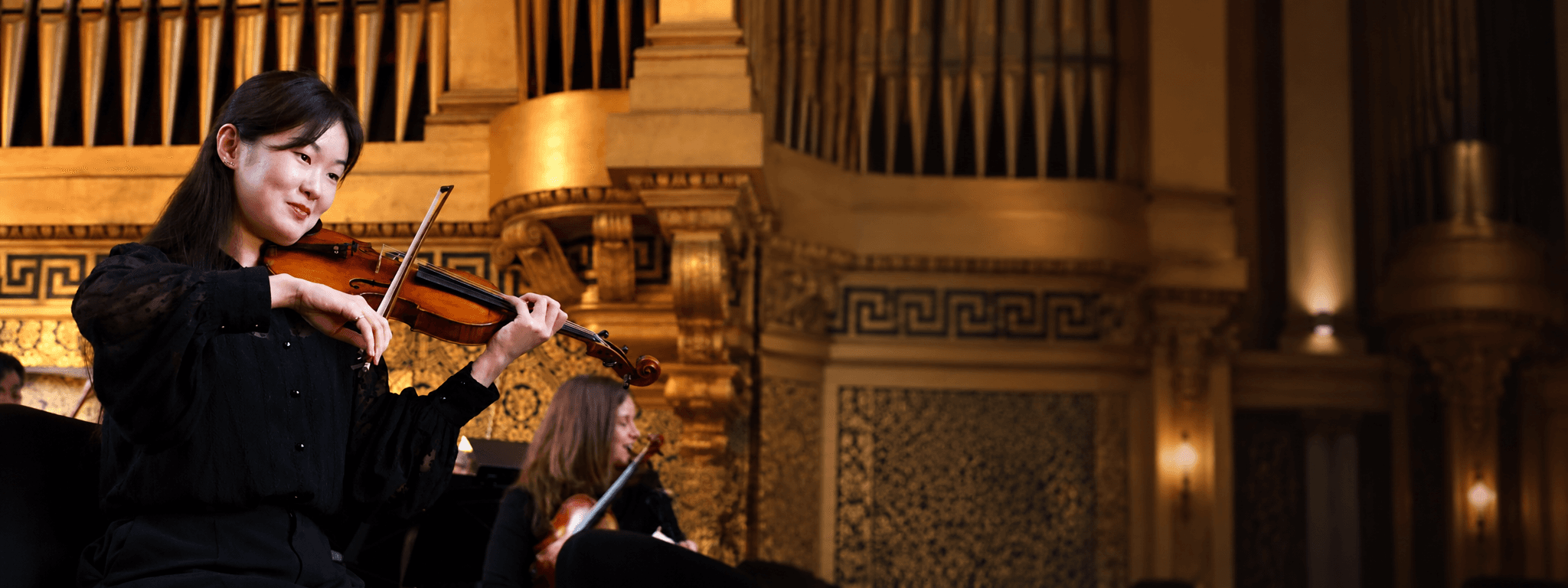 Bin Gui performing violin in a warmly lit concert hall