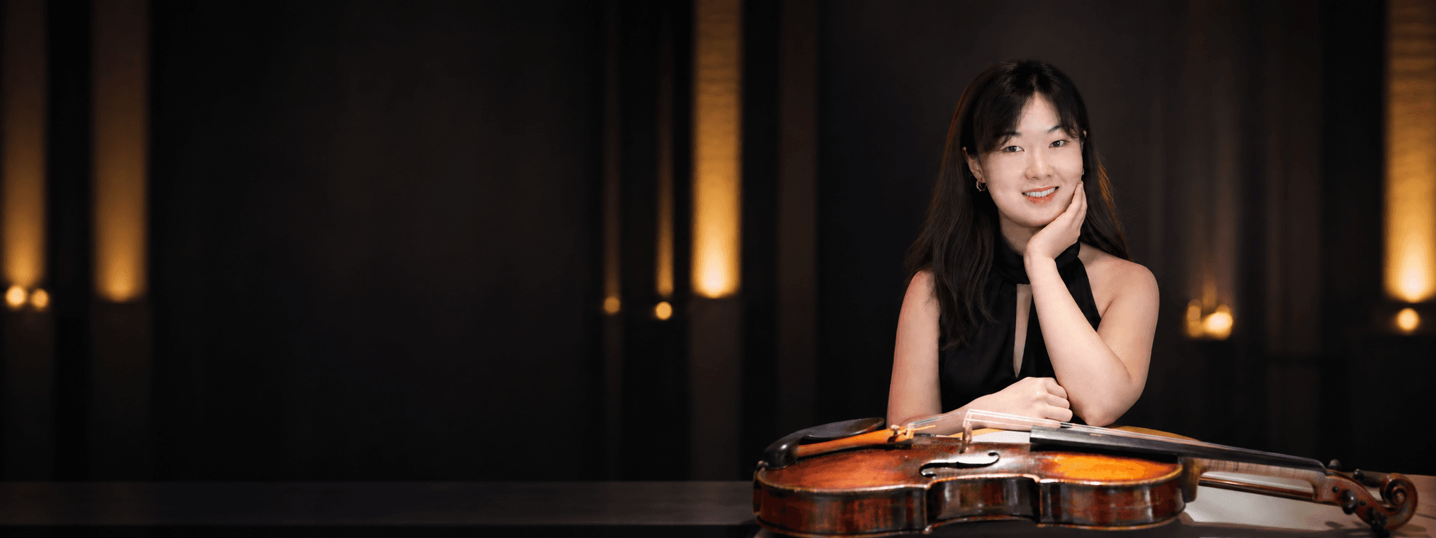Bin Gui seated in a black dress with her violin